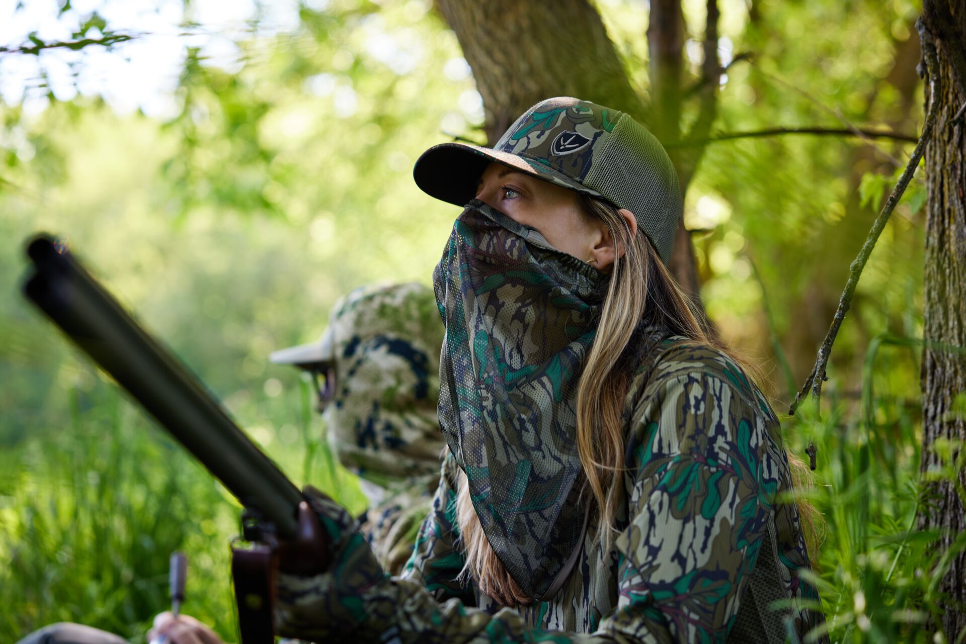 Female hunter in camo with shotgun in the trees, get a Michigan state hunting license concept. 