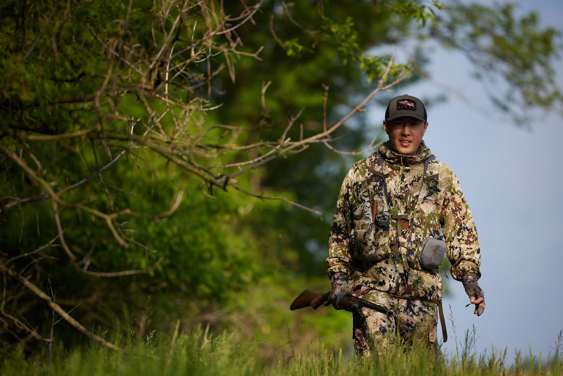 Hunter in camo with shotgun walks treeline, get a Michigan hunting license concept. 