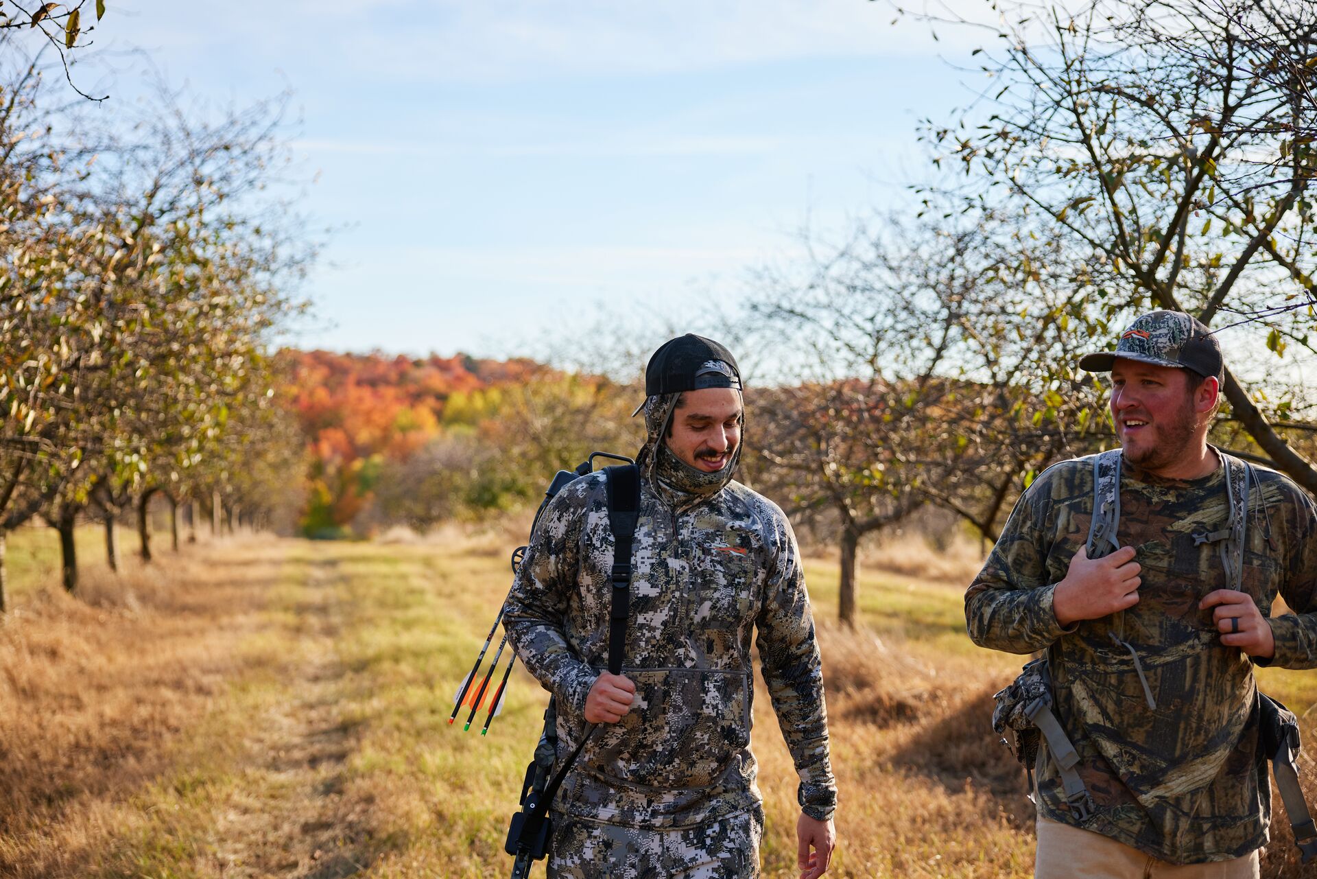 Two hunters in camo walk a trail. 