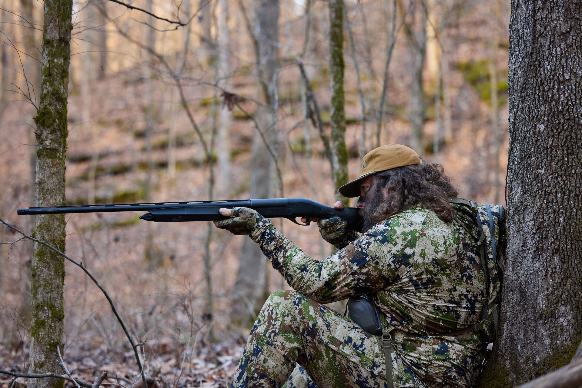 Hunter aims a shotgun while sitting against a tree, know what causes a shotgun to explode concept.