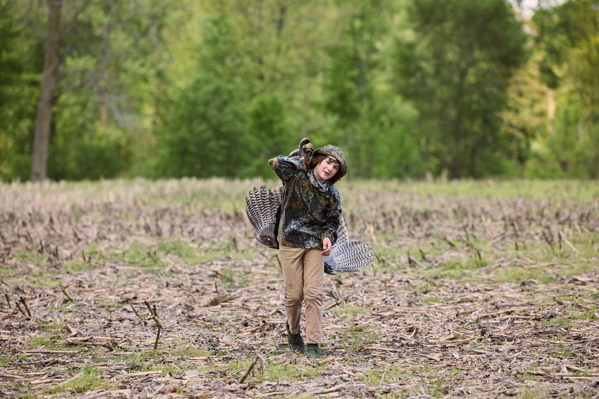 Boy carries turkey in field after hunt, youth hunting license concept. 