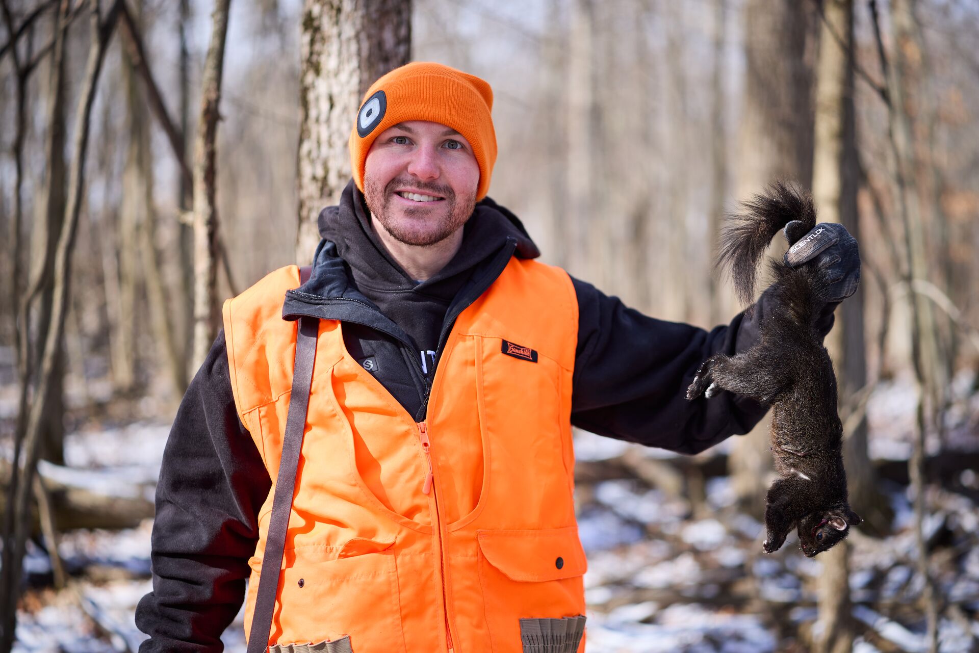 Hunter in blaze orange holds squirrel after hunt. 