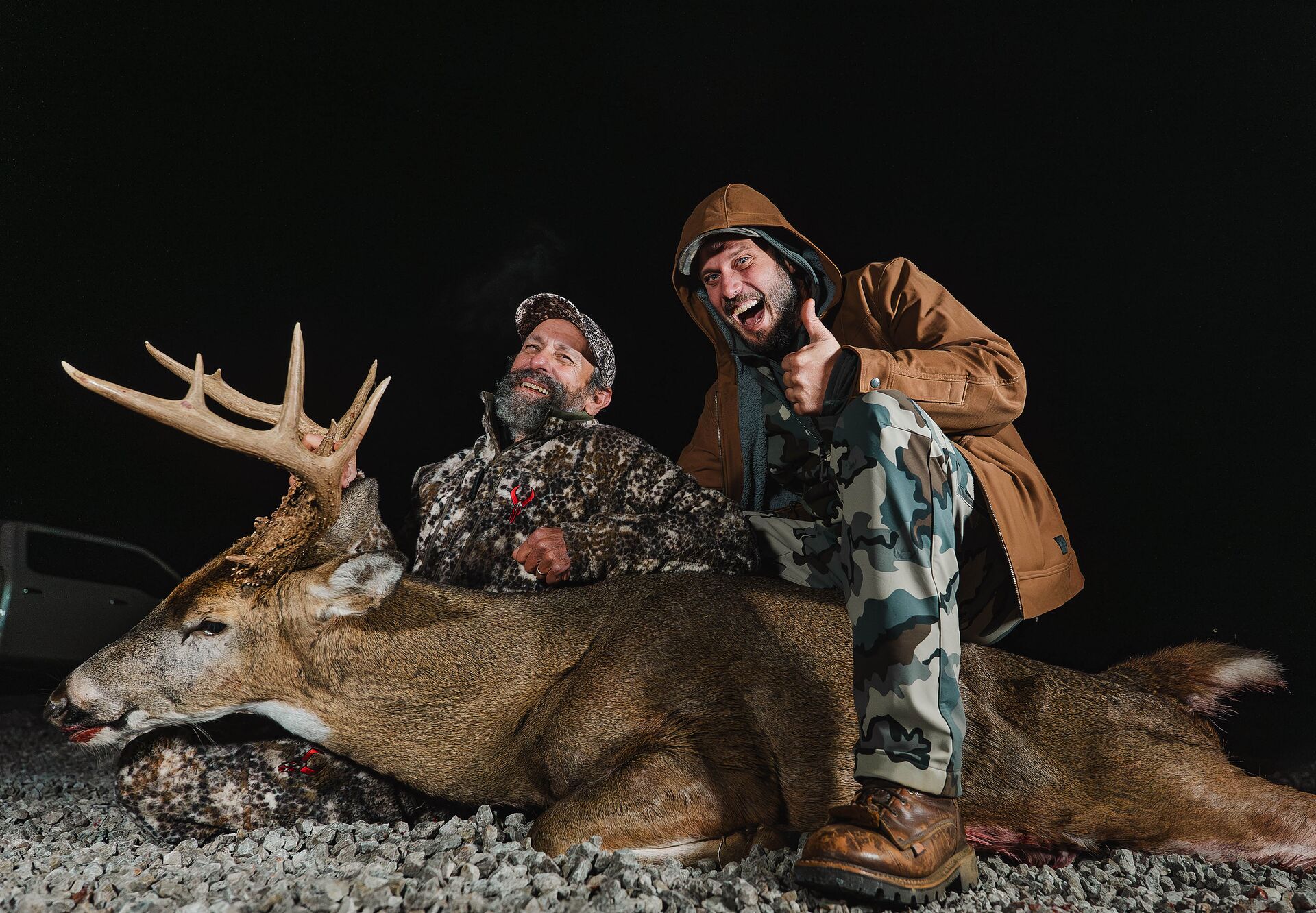 Two hunters smile with thumbs up showing buck deer after hunt. 