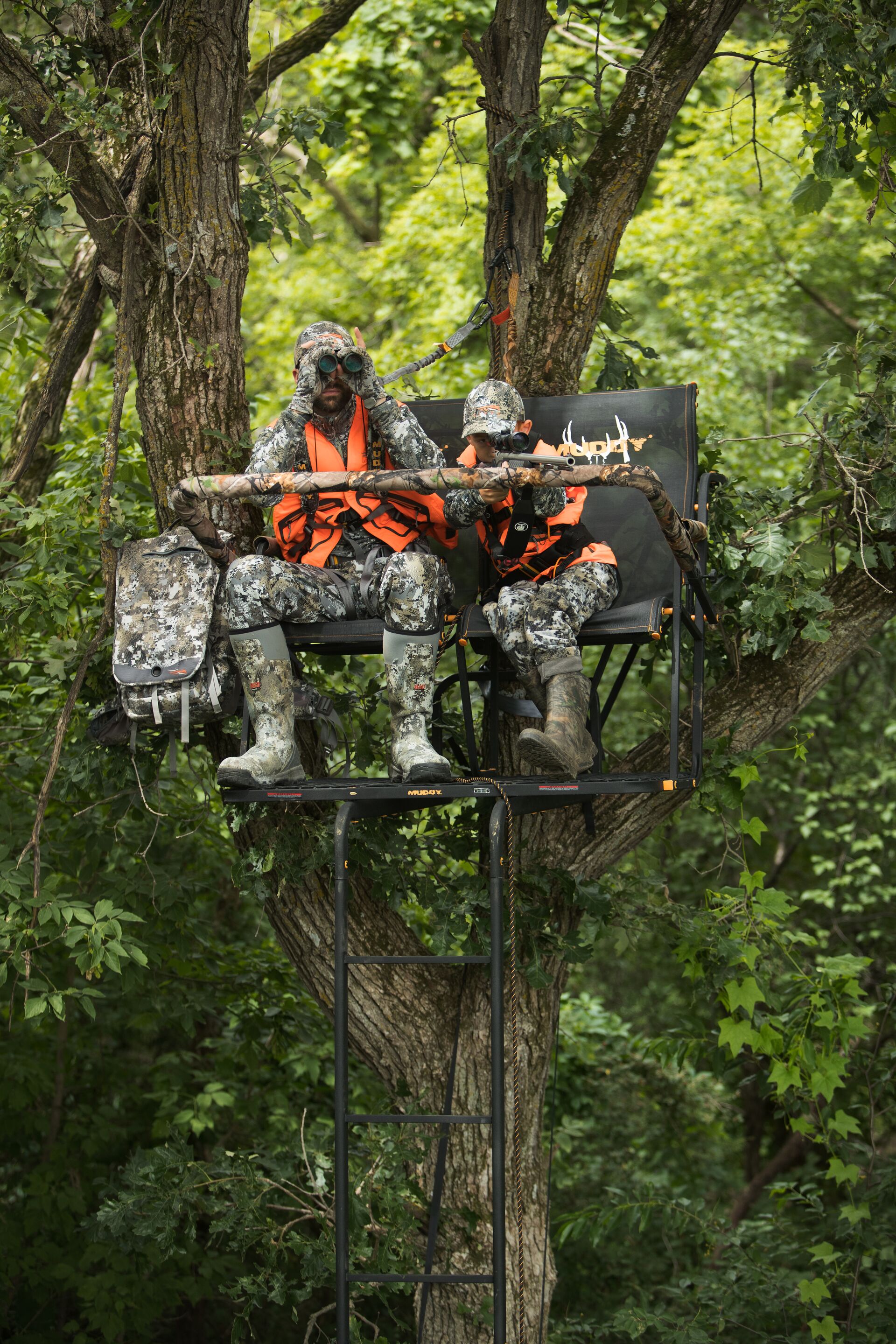 Adult and young hunter use binoculars in tree stand, Louisiana youth hunting concept. 