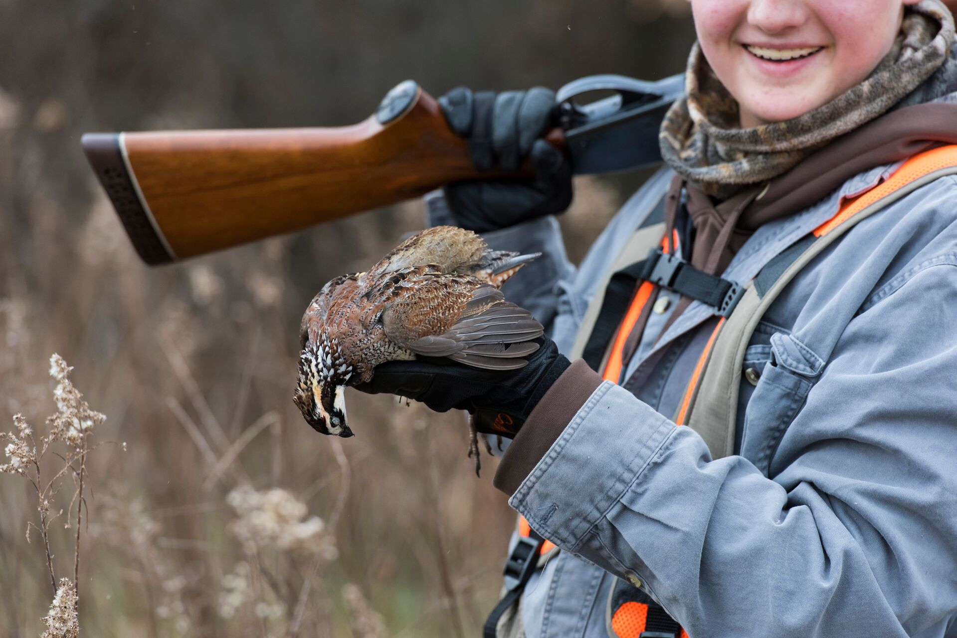Close-up of young hunter holding bird and shotgun after hunt.
