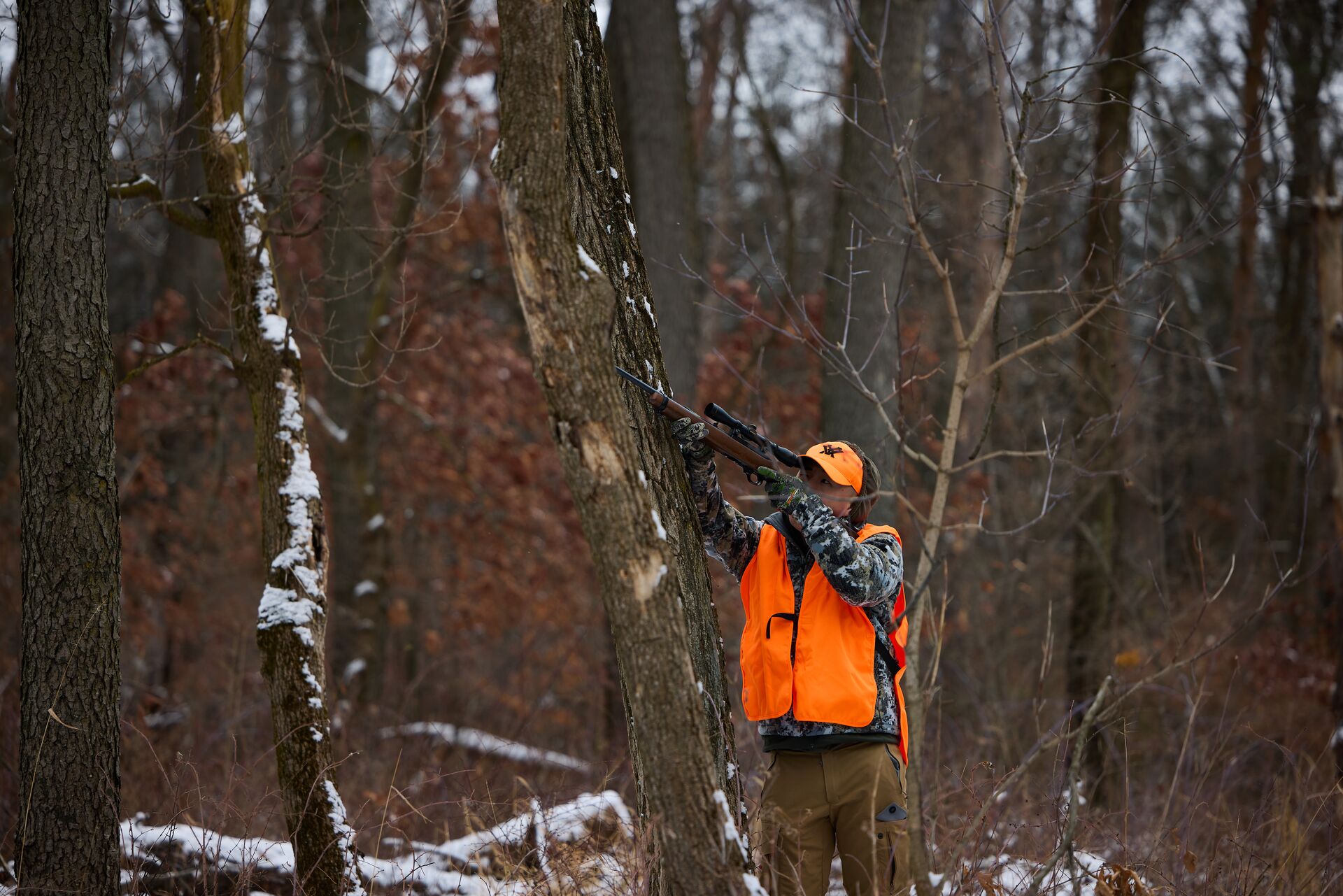 Hunter in orange aims rifle up in the woods, first time hunt concept.
