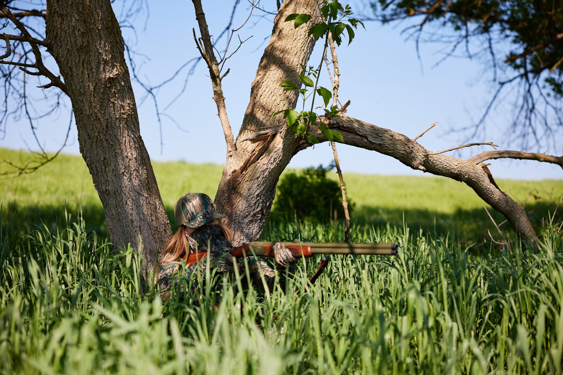 Female hunter in tall grass aims shotgun, take an online hunter safety course concept. 