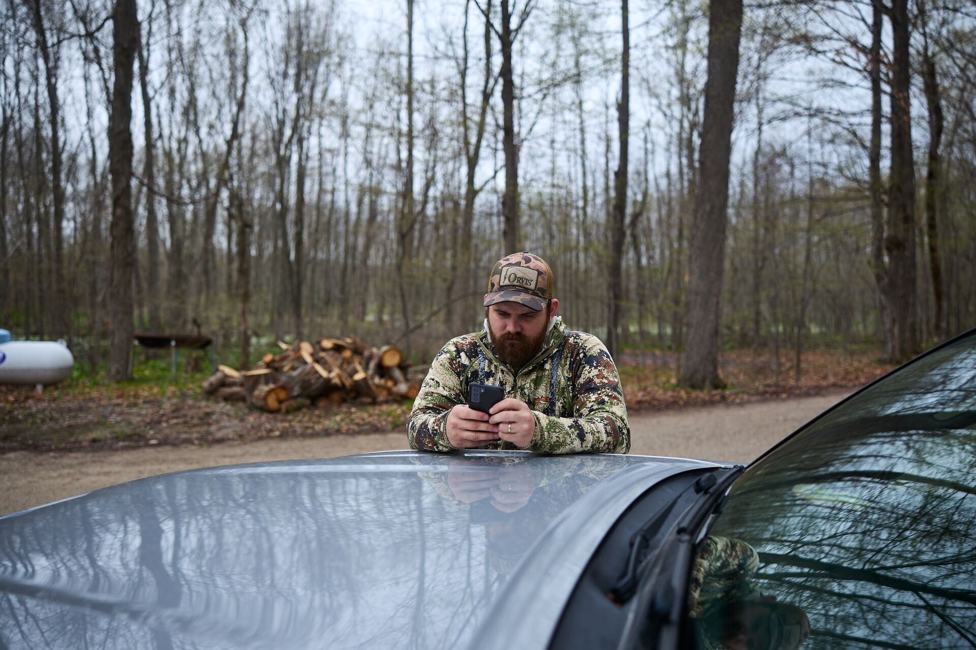 Hunter leans on truck using phone, take an online hunter safety course concept. 