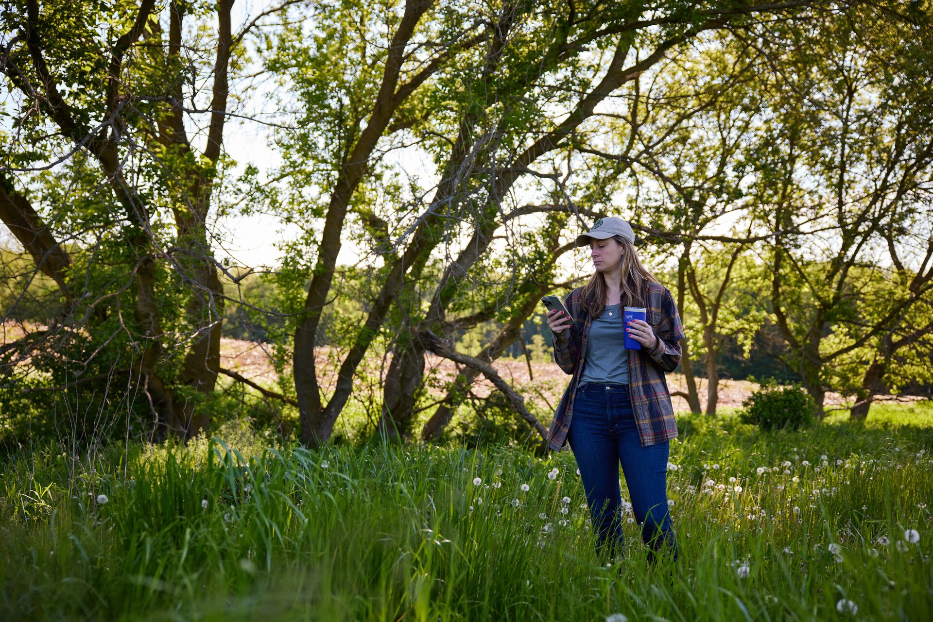 Woman uses phone while standing near trees, online hunting safety concept.