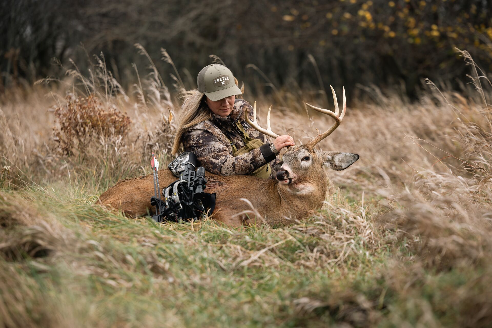 Female hunter sits with deer and bow after hunt, complete online hunter safety course concept.