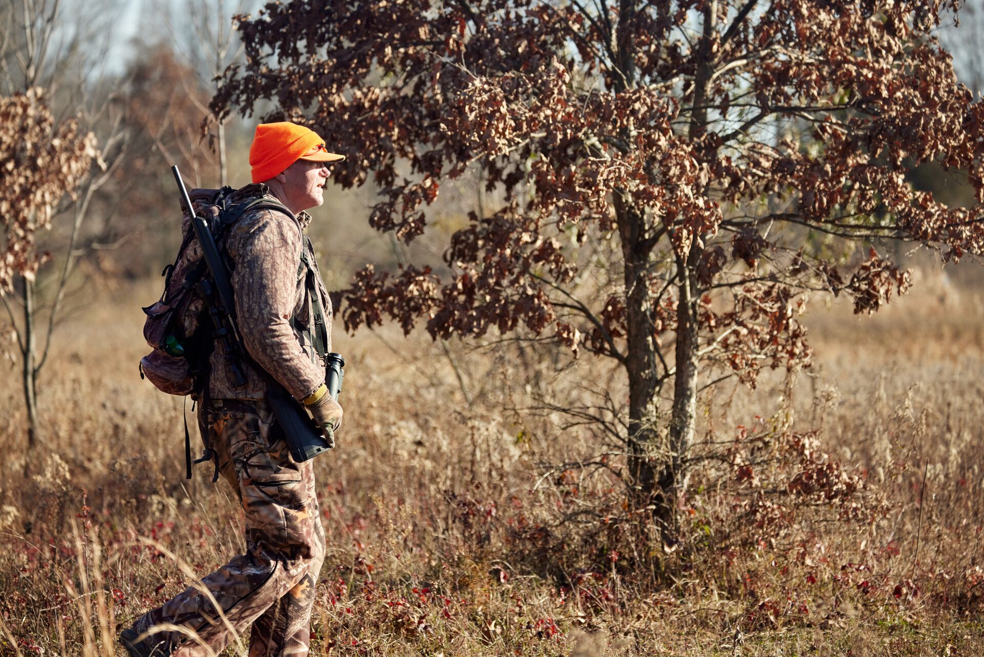 Man in blaze orange hat walks in woods, where to take the DE hunter safety course concept. 