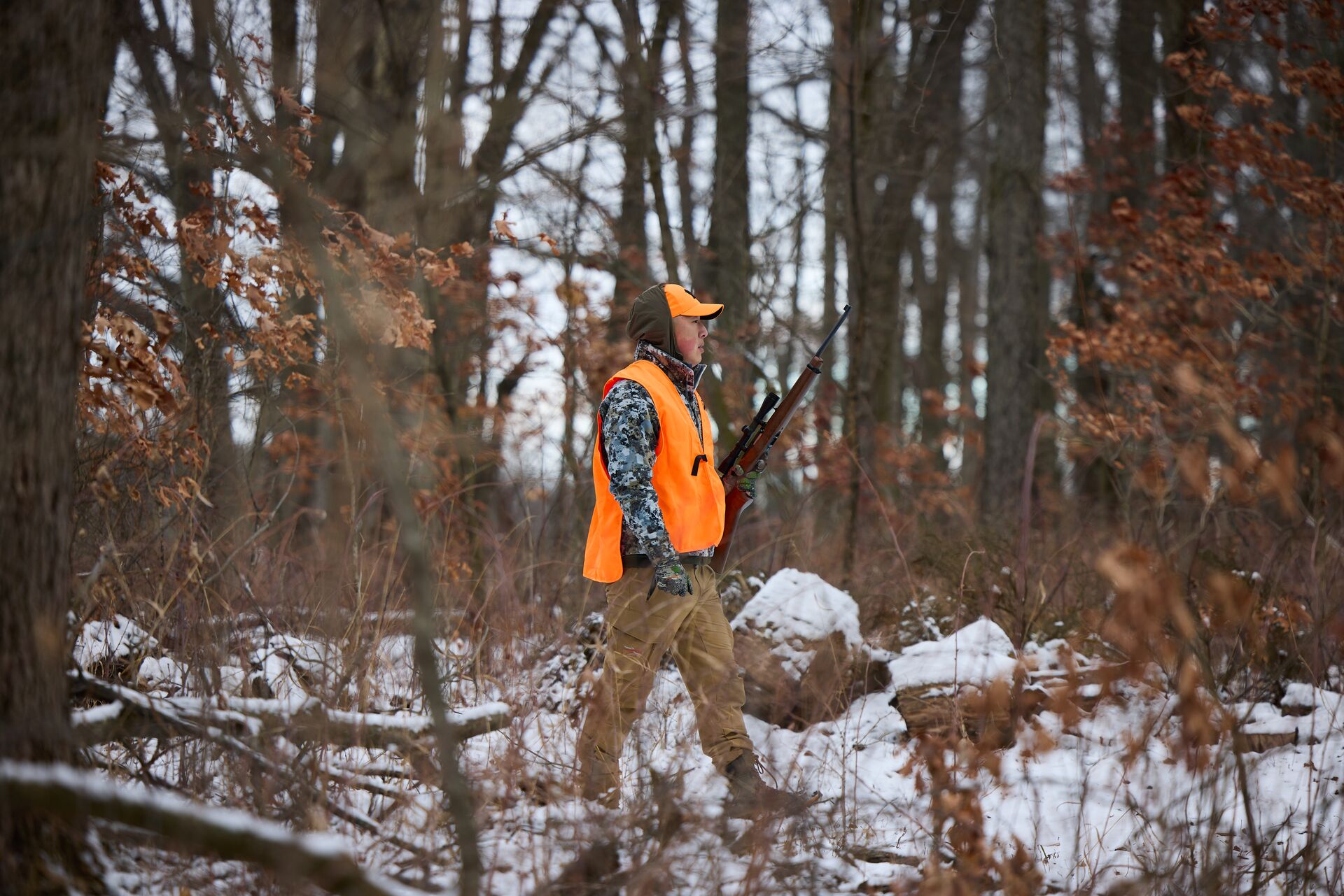 Hunter in blaze orange with rifle in the woods, hunter safety course cost concept.
