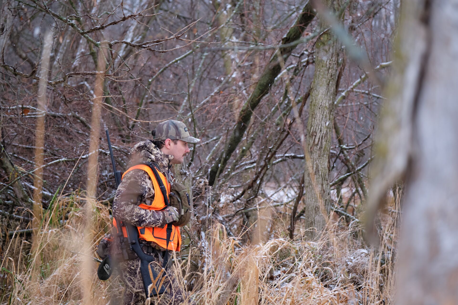 Hunter in blaze orange walks in the woods, what is a hunter safety course concept.