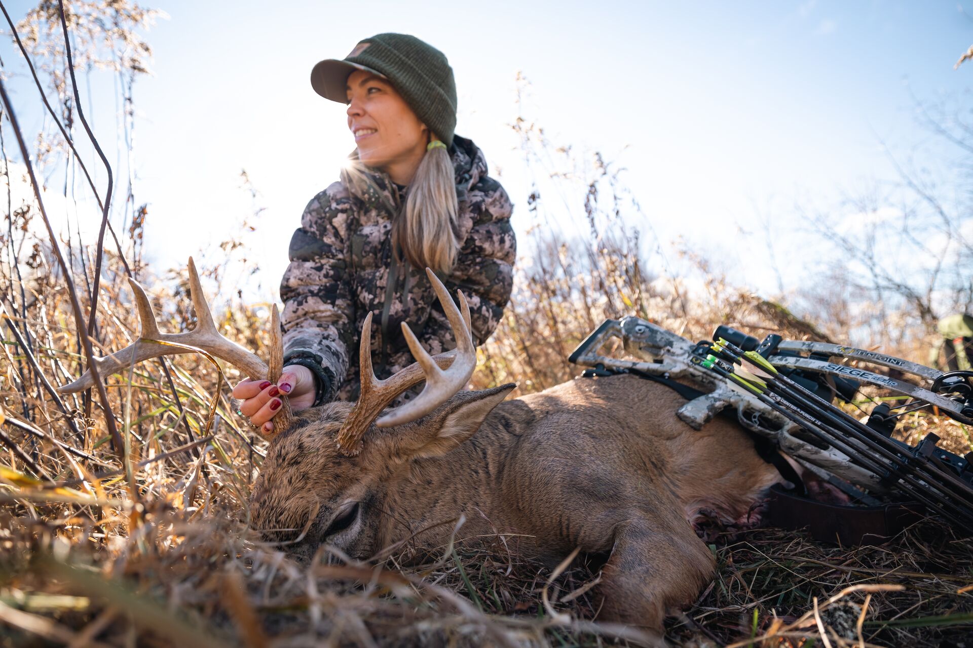 Woman smiles with buck deer on ground after hunt, learn to hunt as adult concept. 