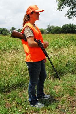 A female hunter in blaze orange using elbow carry for her shotgun.