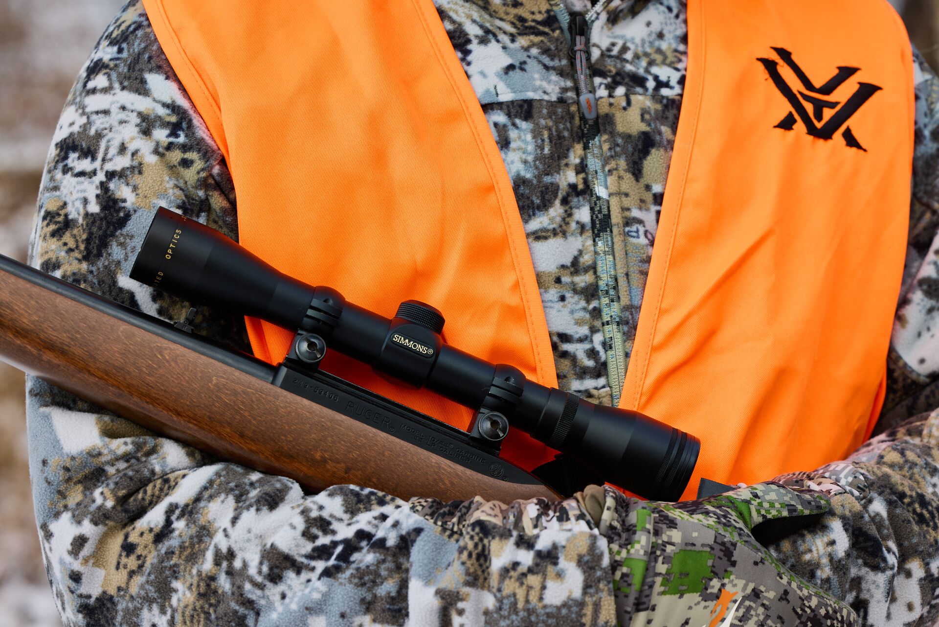 Close-up of a hunter in camo and a blaze orange vest with a rifle, hunting safety tips concept.