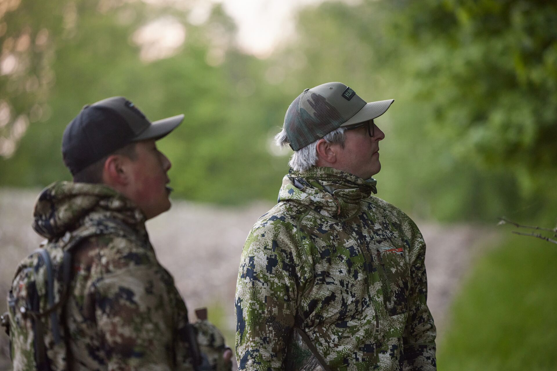 Two hunters in camo looking toward the woods. 