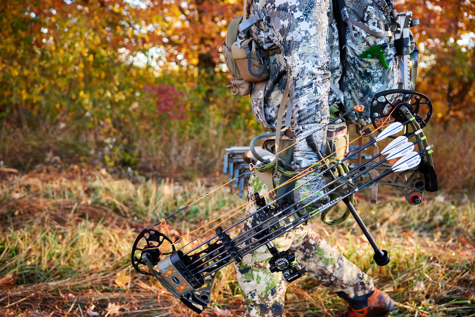 A hunter carries a compound bow through the woods.