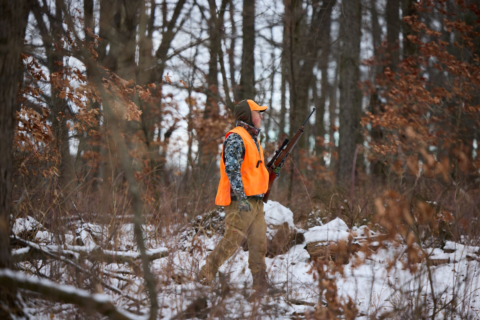 A hunter walks in the woods while wearing hunter orange.