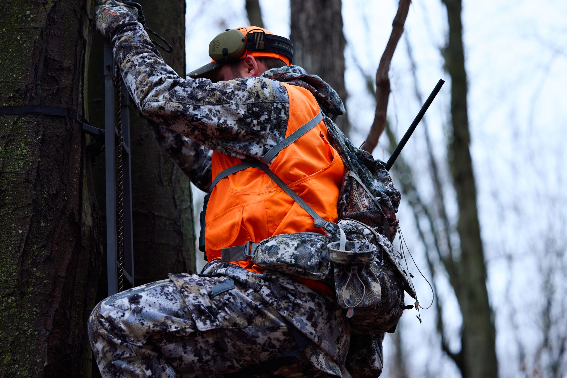 Hunter in camo and blaze orange climbs into tree stand.