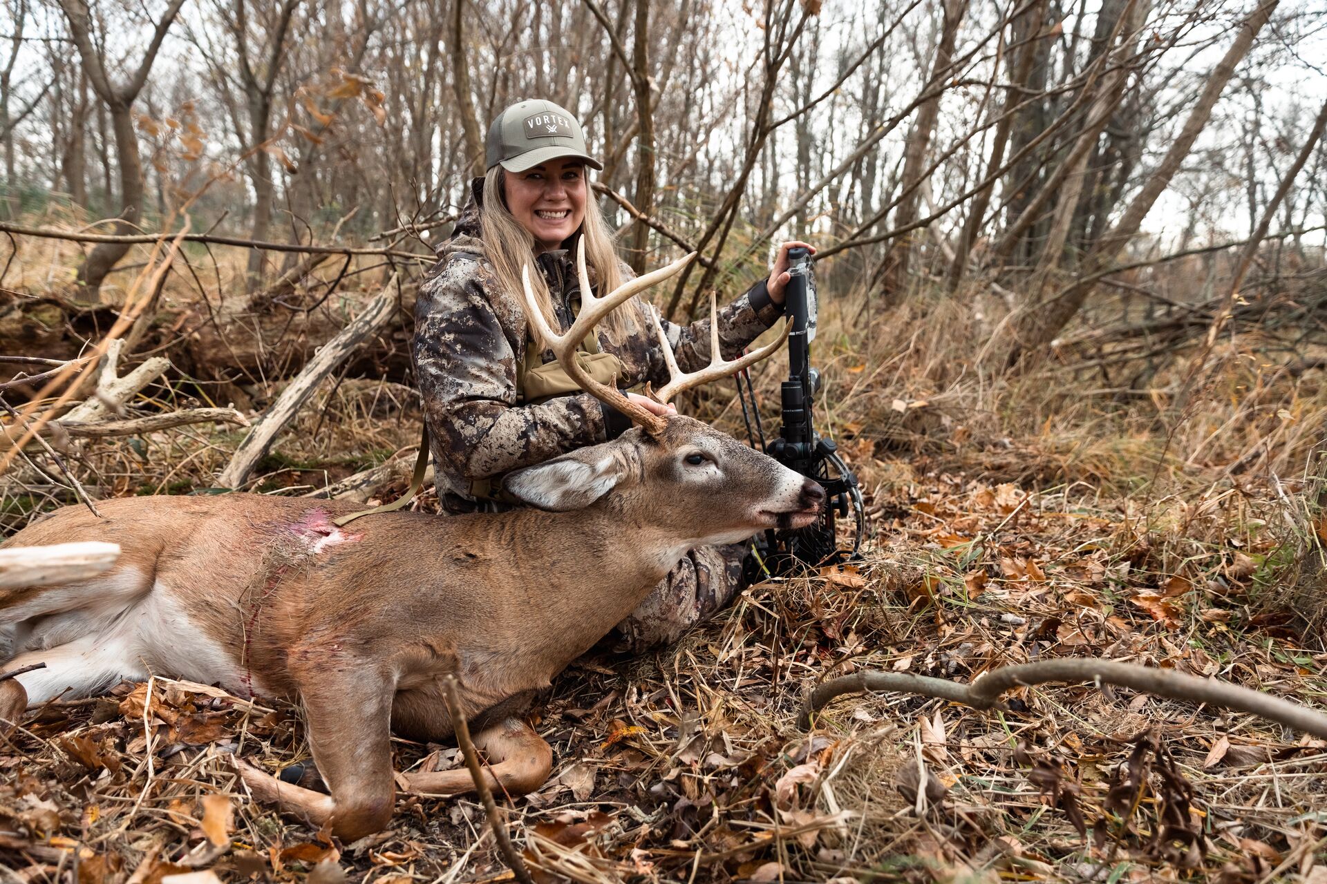 Smiling woman with a downed deer, broadside shot concept.