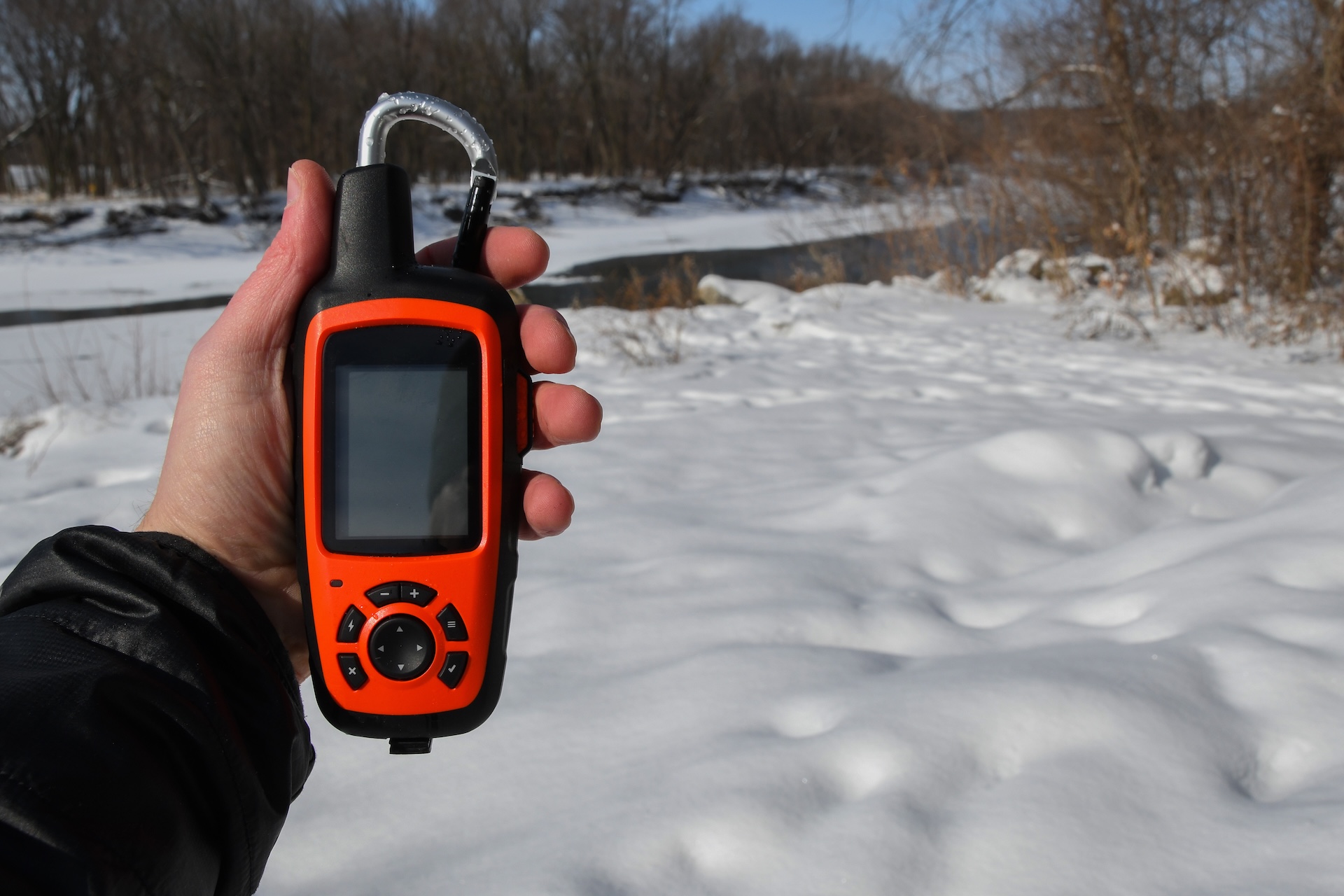Hand holding a GPS device in the snowy woods. 