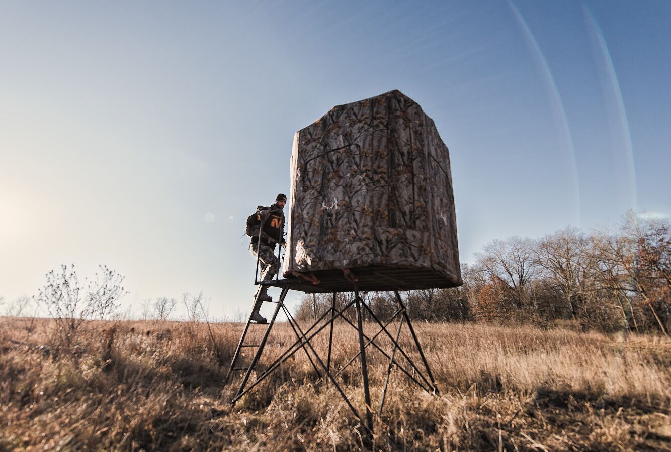 Hunter climbing into hunting blind in field. 