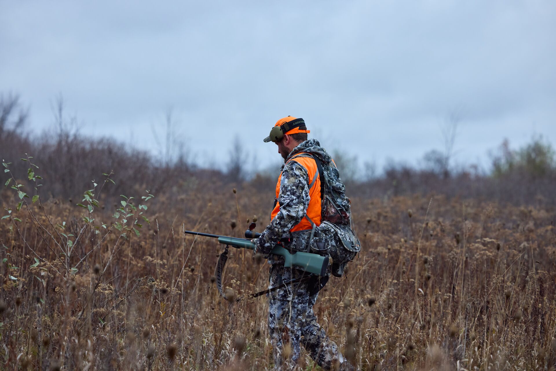 Hunter in camo and blaze orange with rifle, how to start hunting concept.