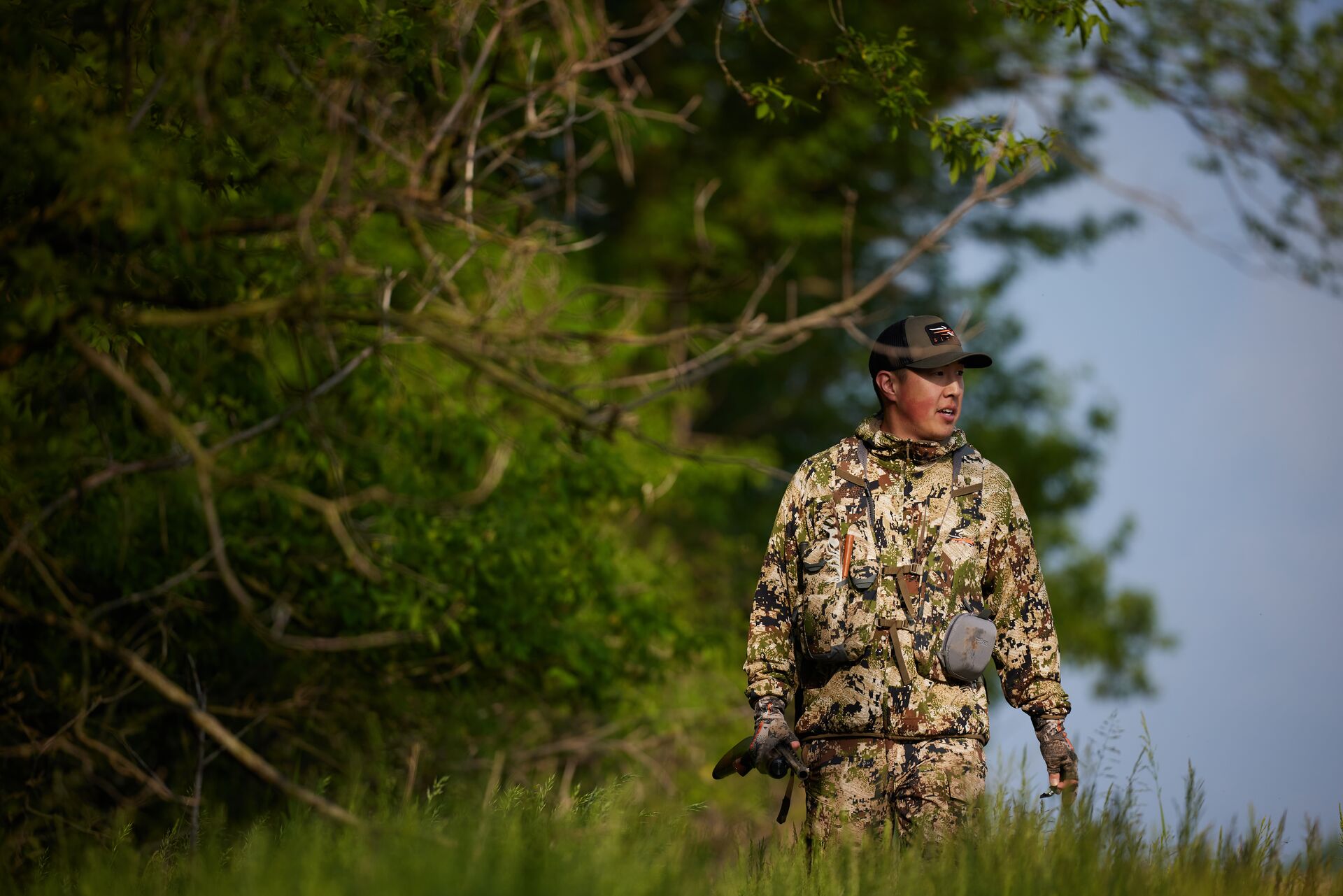 Hunter in camo with firearm near trees, how do I get into hunting concept.