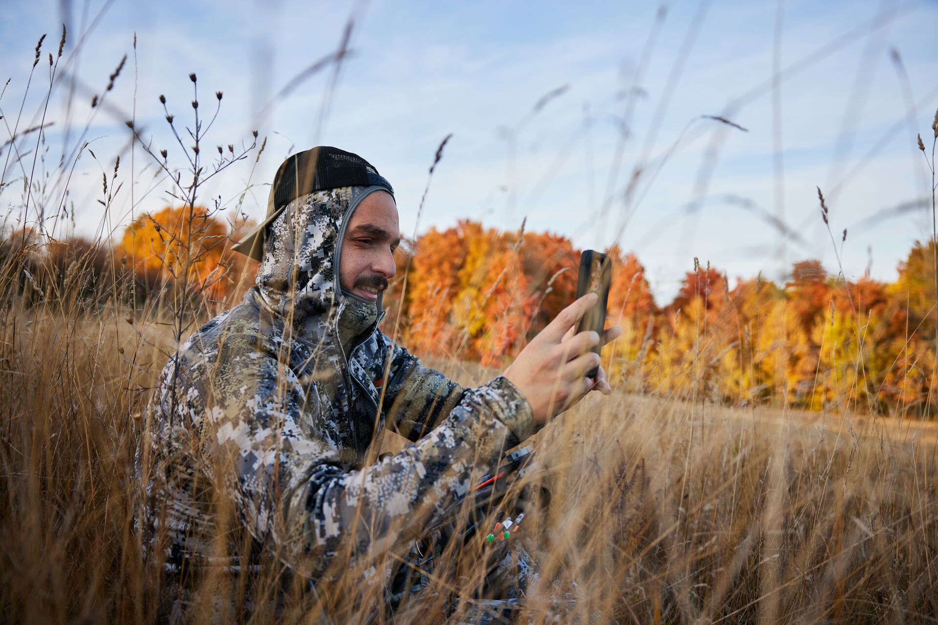 Hunter in a field looks at a phone to scout. 