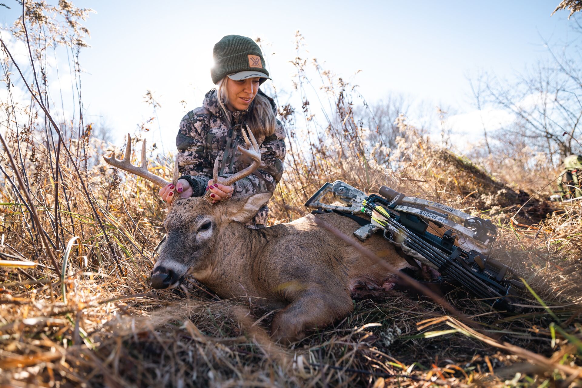Female hunter sits with deer on the ground after hunt.