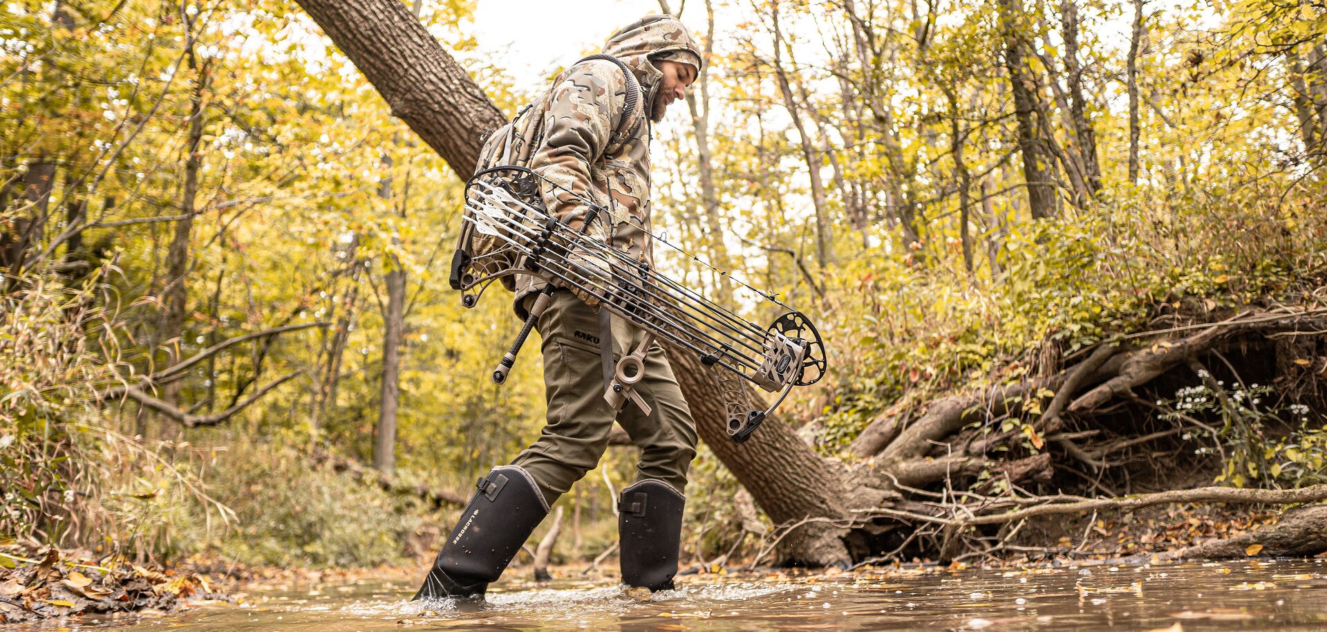 Hunter walks through water carrying bow.