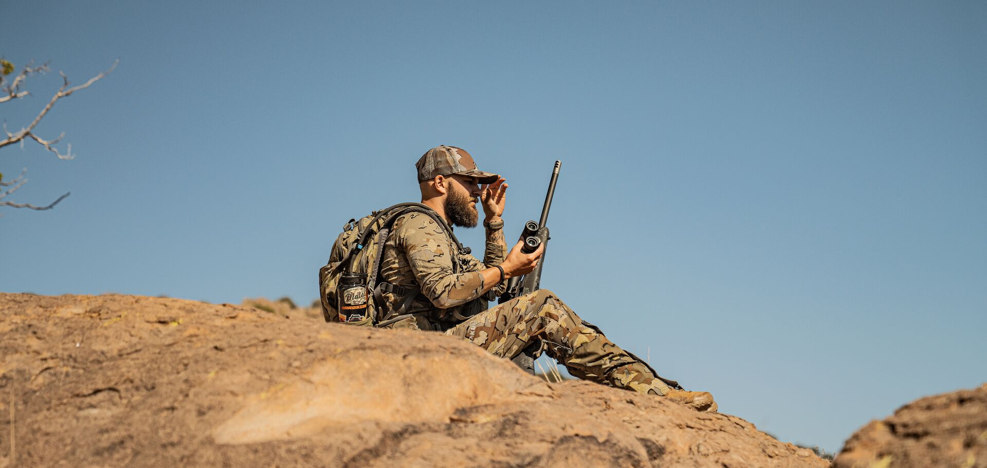 Hunter on rock with binoculars and rifle, long range rifle calibers concept. 