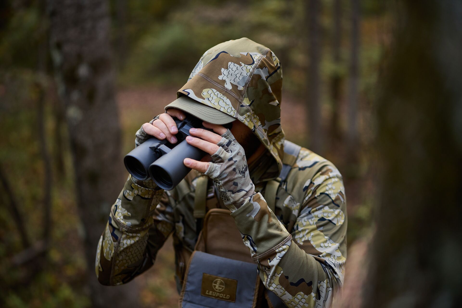 Hunter in camo uses binoculars outdoors, scouting for hunting concept. 