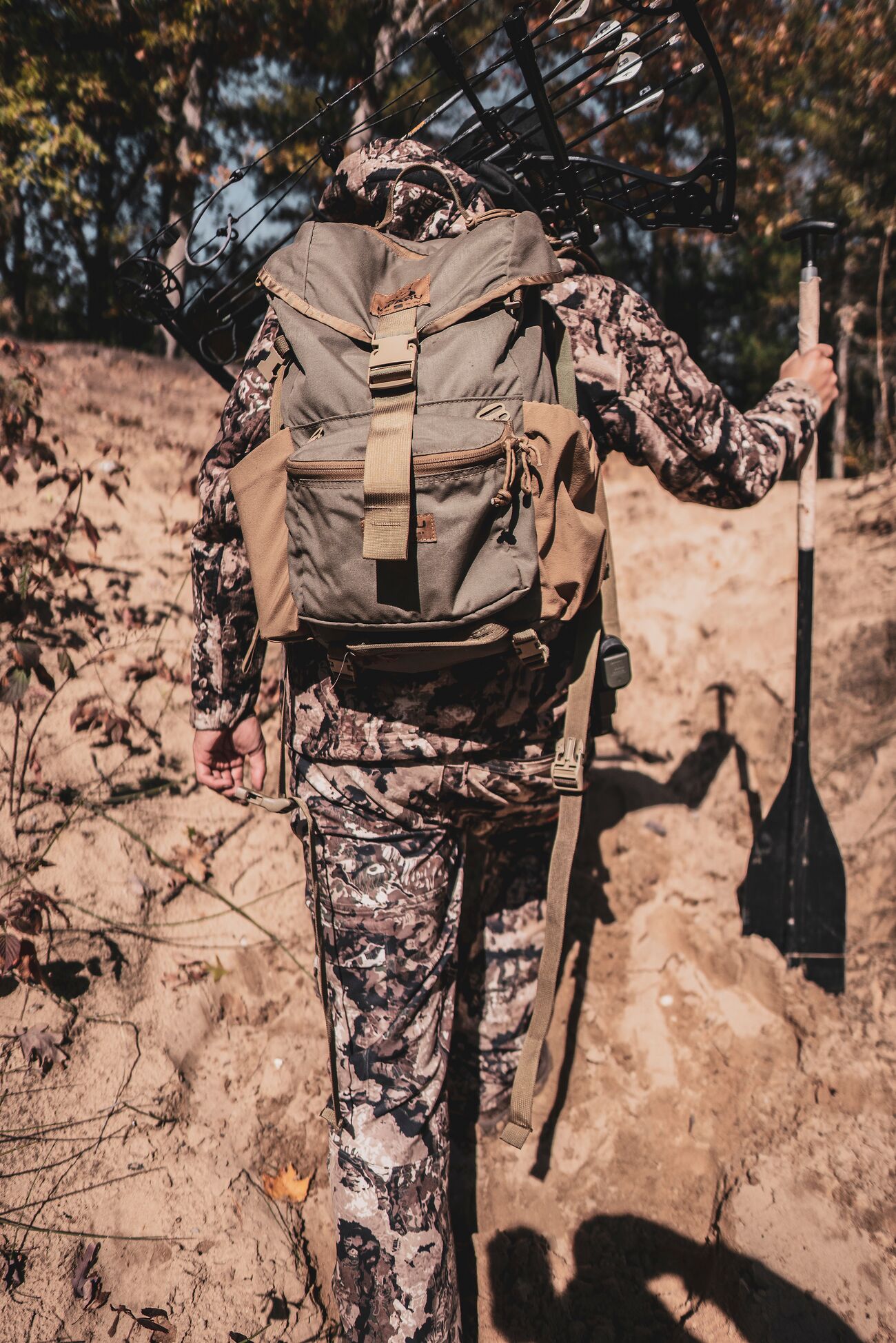 Hunter wearing camo and gear hikes over rocks.