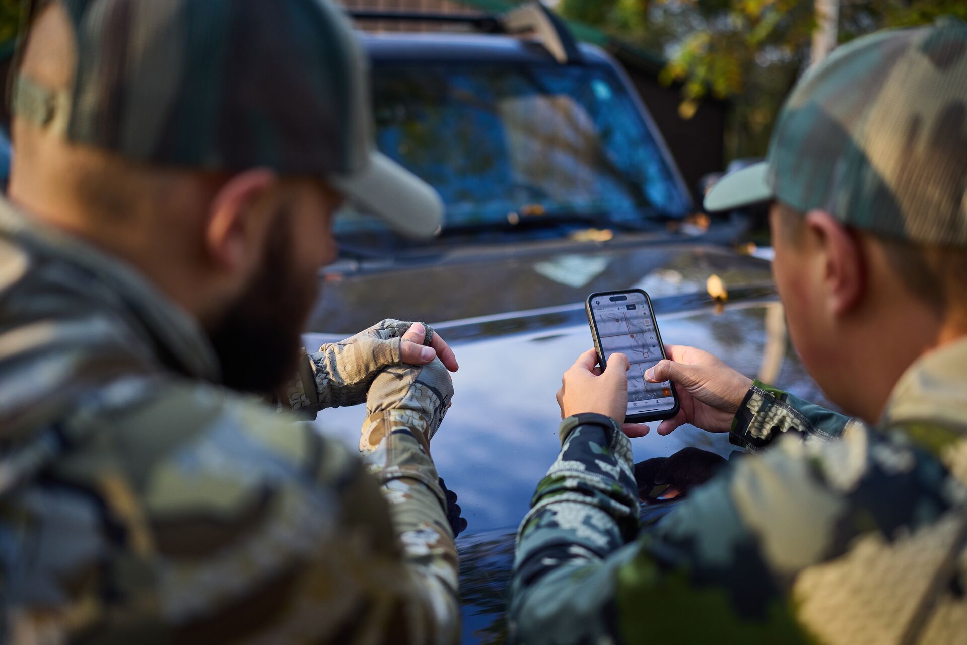 Two hunters lean on truck while looking at phone, hunting plan concept.