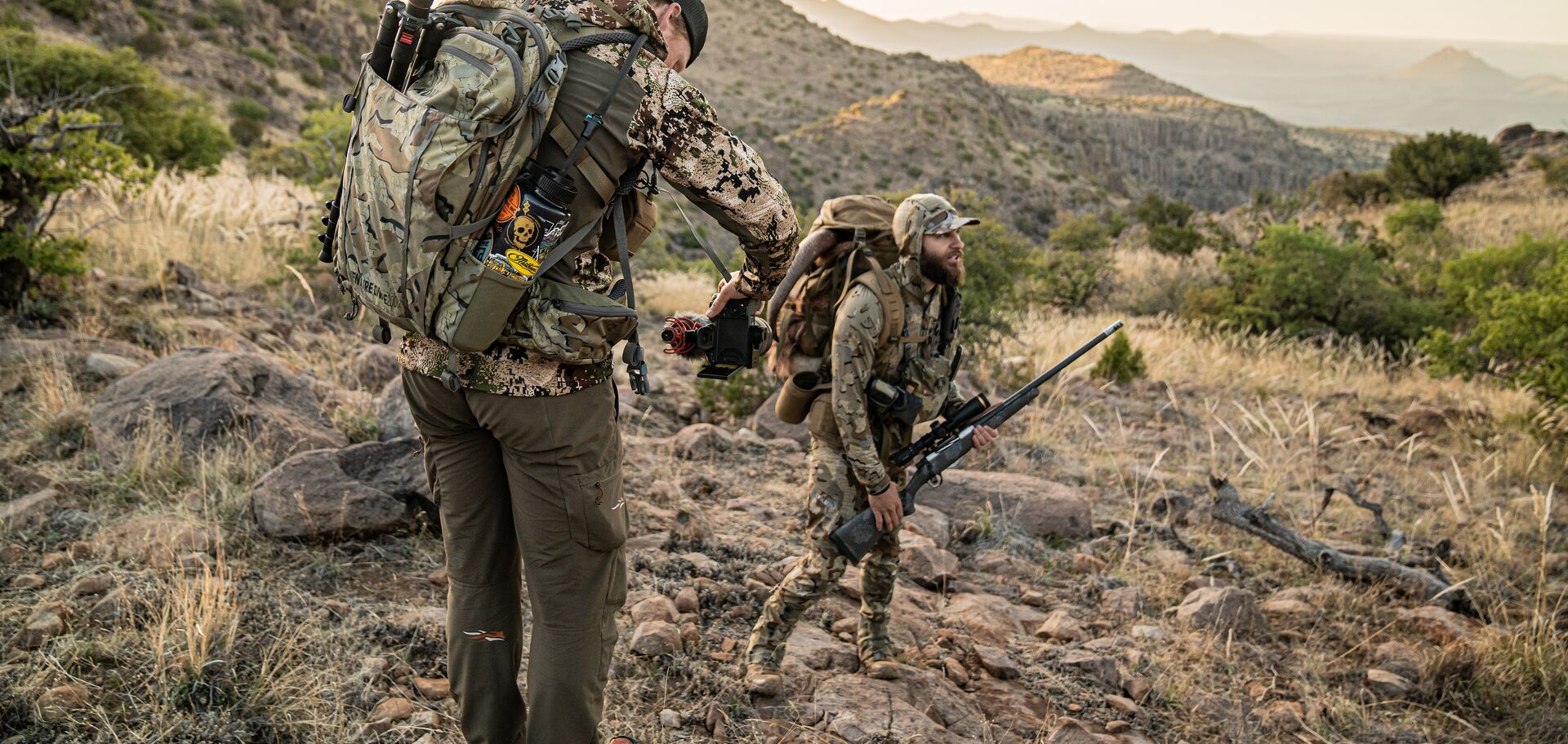 Two hunters with rifles and gear for hunt.