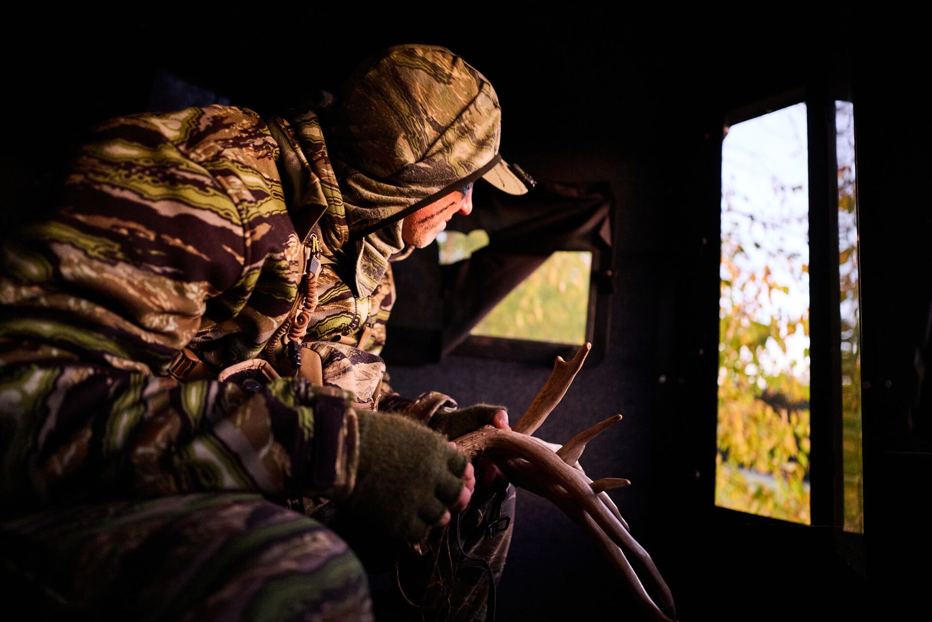 Hunter in ground blind rattles antlers, represents ground blind hunting strategies.